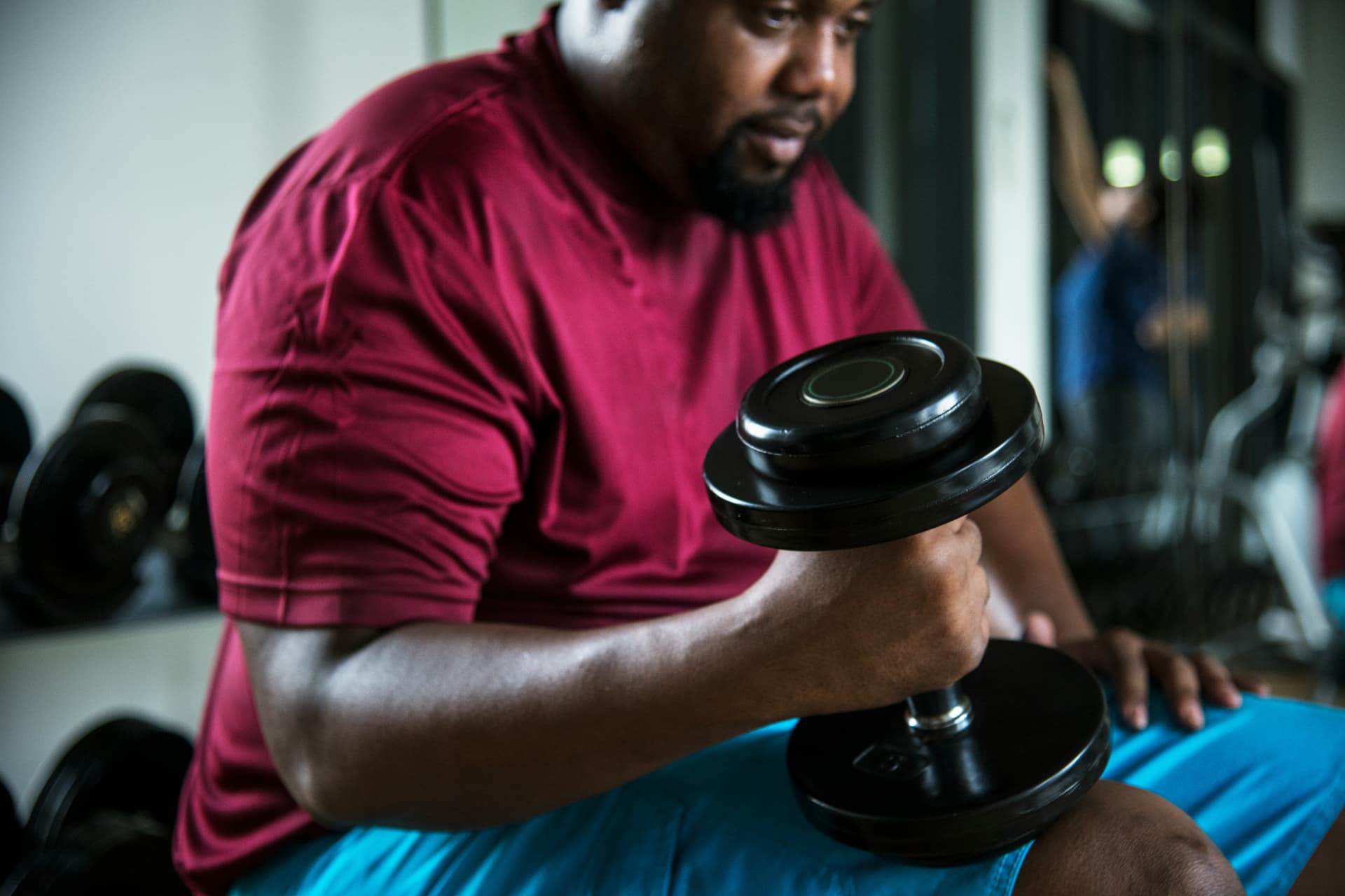 Man in a red shirt curling a dumbbell while seated in a gym