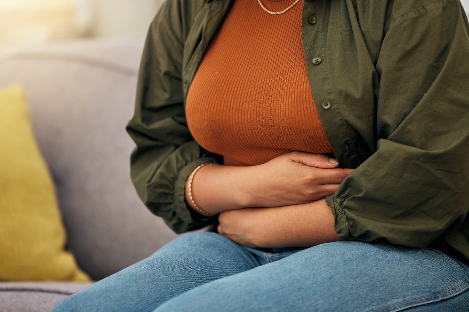 Close-up of a woman sitting on a sofa holding her stomach with both hands