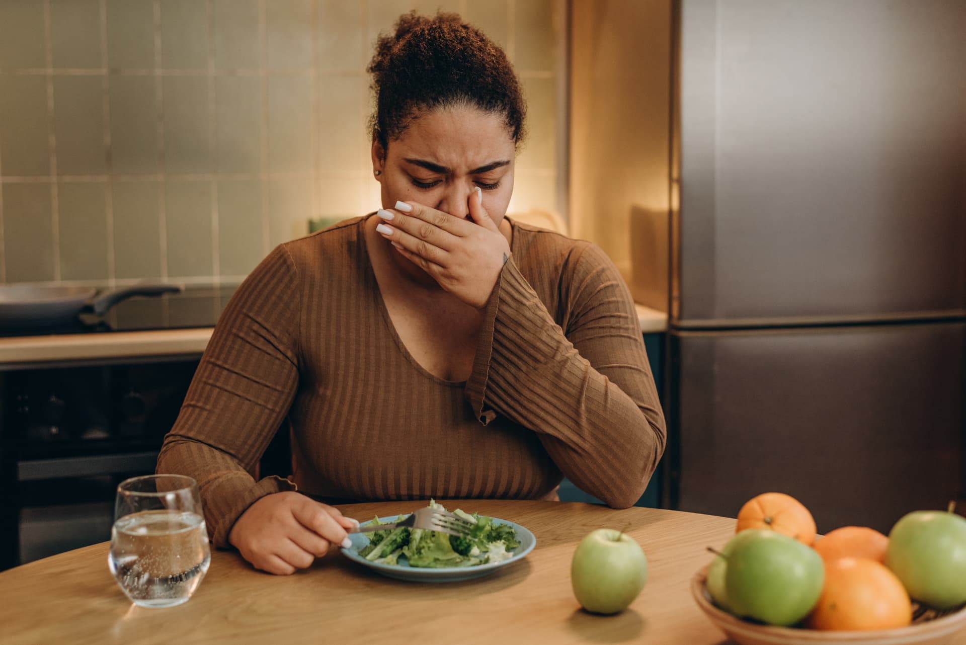 Woman at a kitchen table covering her mouth with her hand in front of a plate of salad