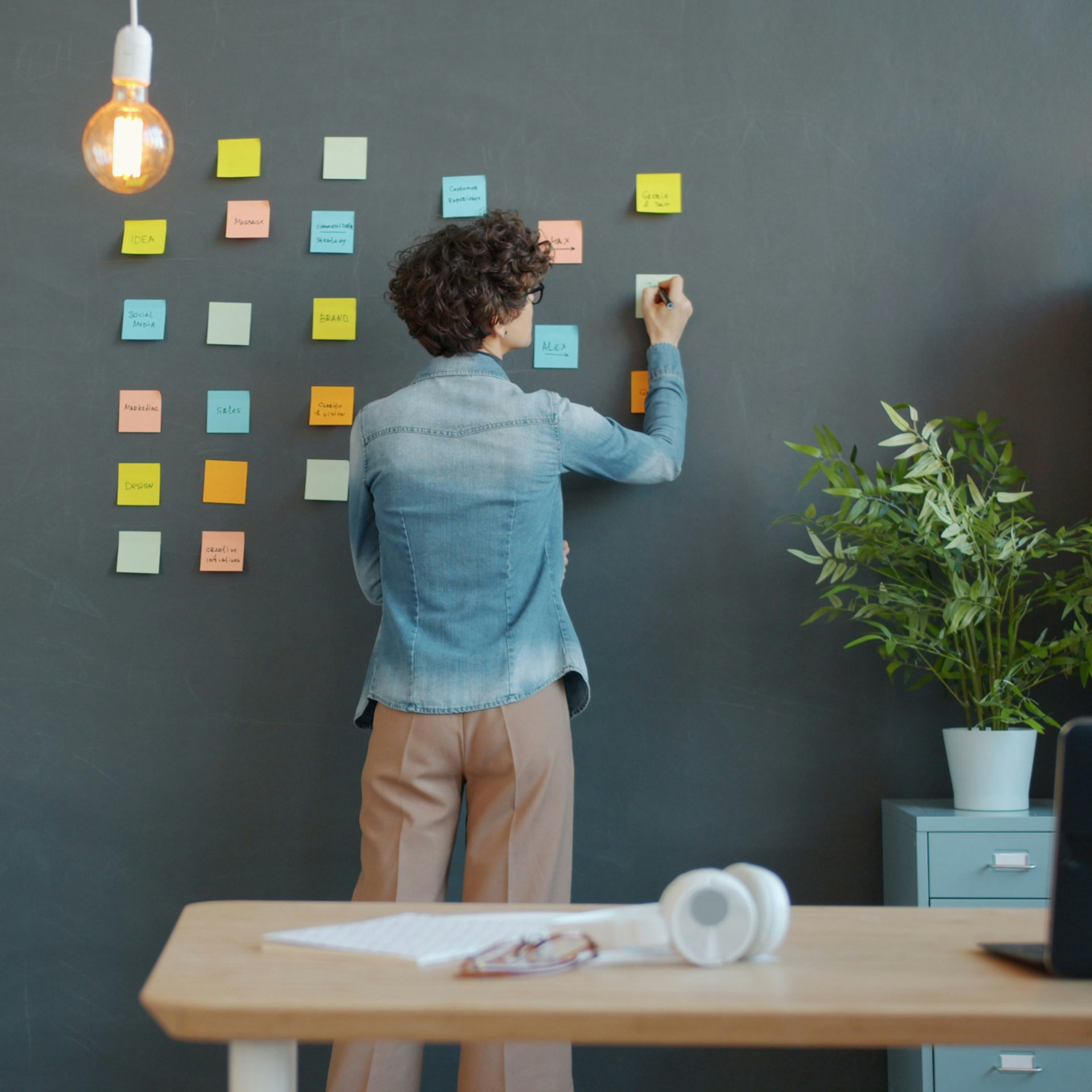 Woman writing on colorful sticky notes arranged on a dark wall