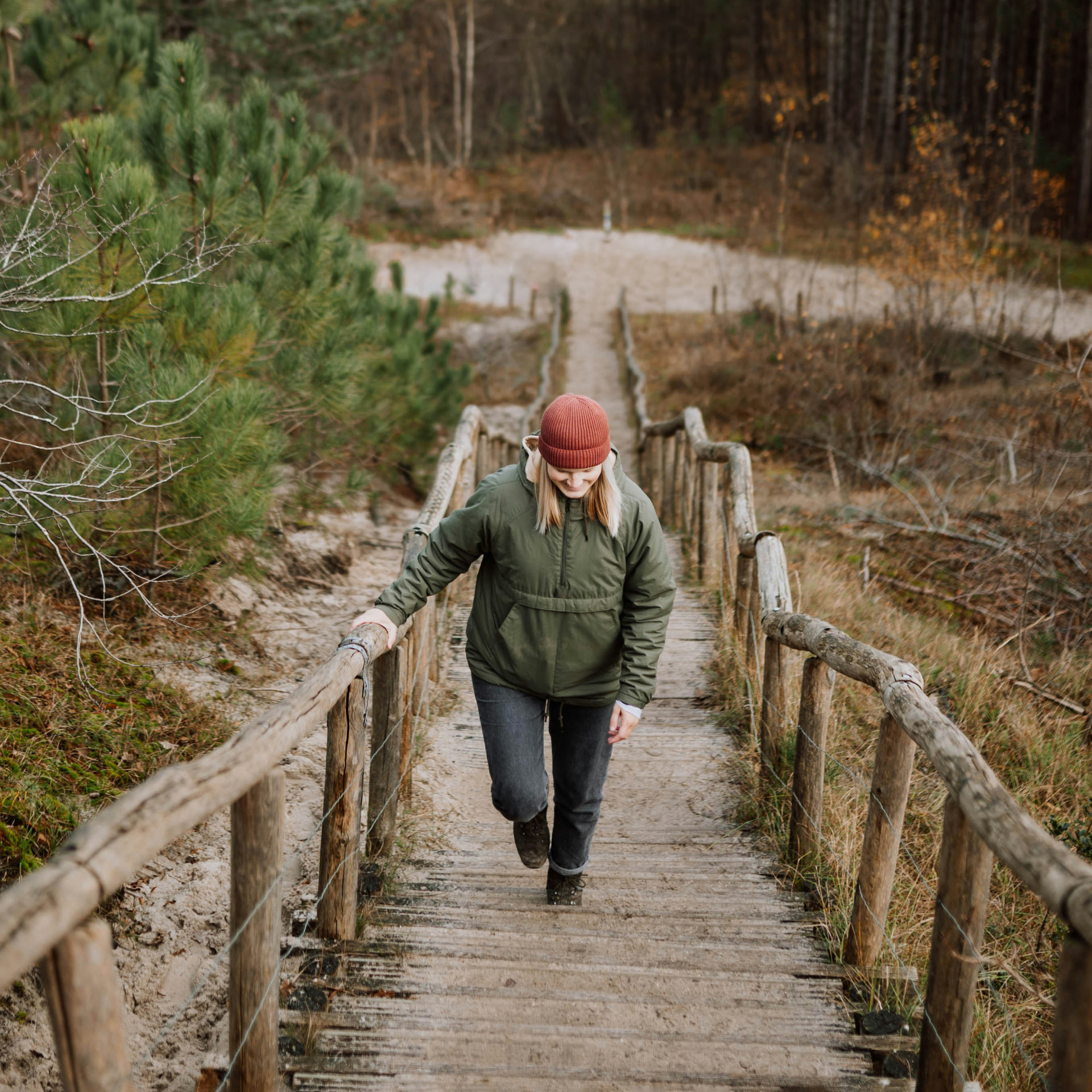 Woman in a green jacket and knit hat climbing wooden steps on a sandy forest trail